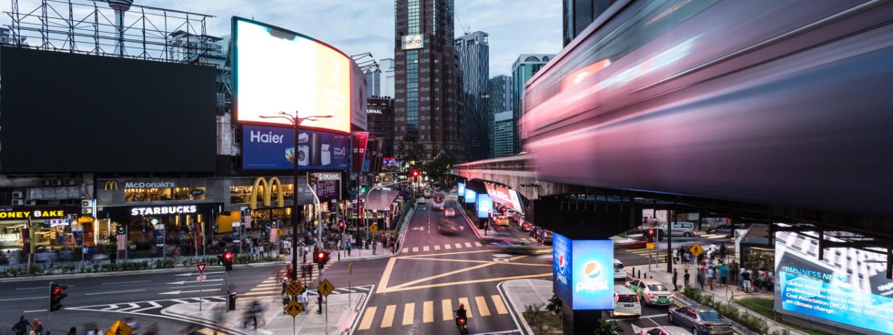 Traffic and a monorail car rush through the Bukit Bintang intersection at night in Kuala Lumpur, Malaysia capital city.